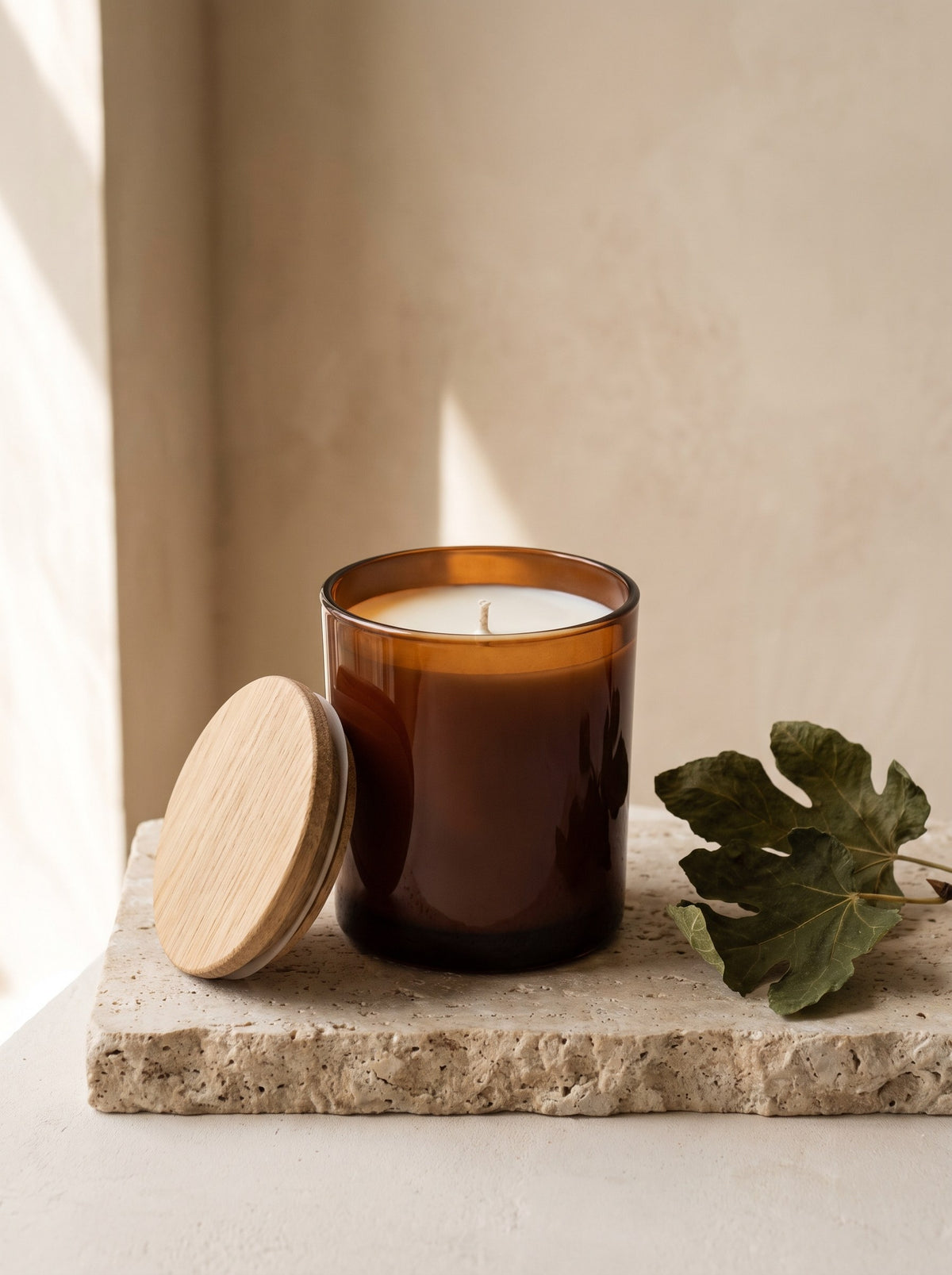 Amber & Fig Soy Candle in an amber glass jar with its oak lid on a travertine plinth