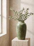 Moss green reactive glaze ceramic vase with olive branches on a travertine plinth