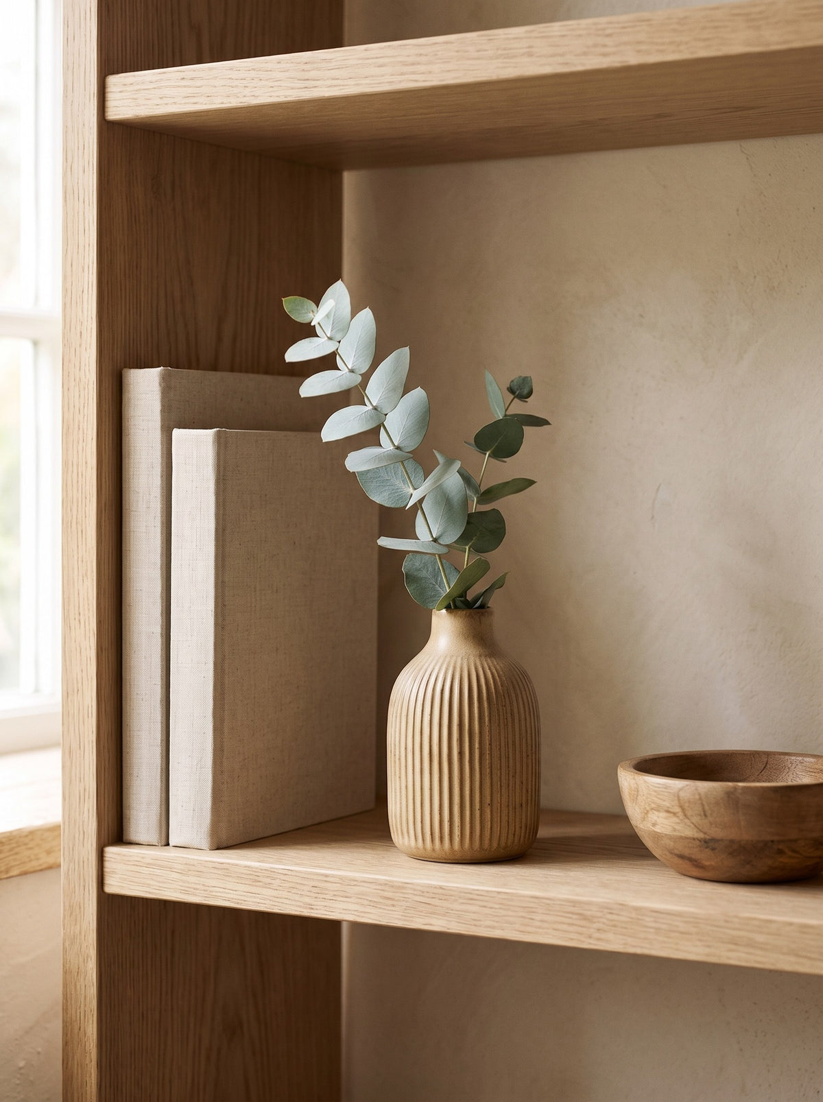 Sand Ribbed Stoneware Bud Vase with a eucalyptus sprig on an oak shelf beside books