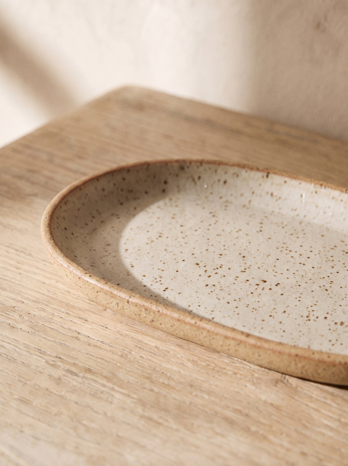 Close-up of the brown speckles and raw clay rim of the oatmeal stoneware tray