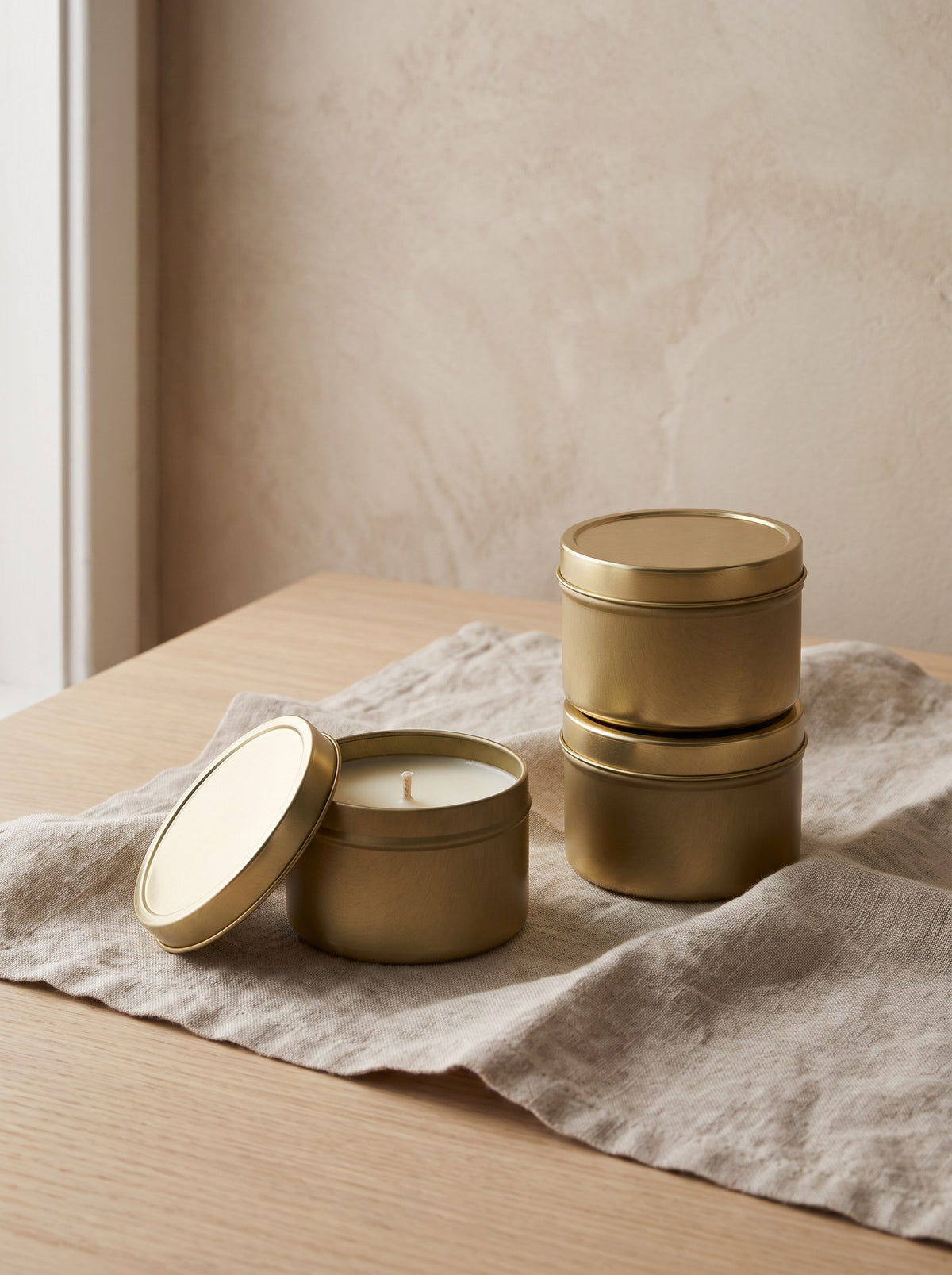 Travel Tin Candle Trio - three brushed brass-tone tin candles on a linen cloth, one open