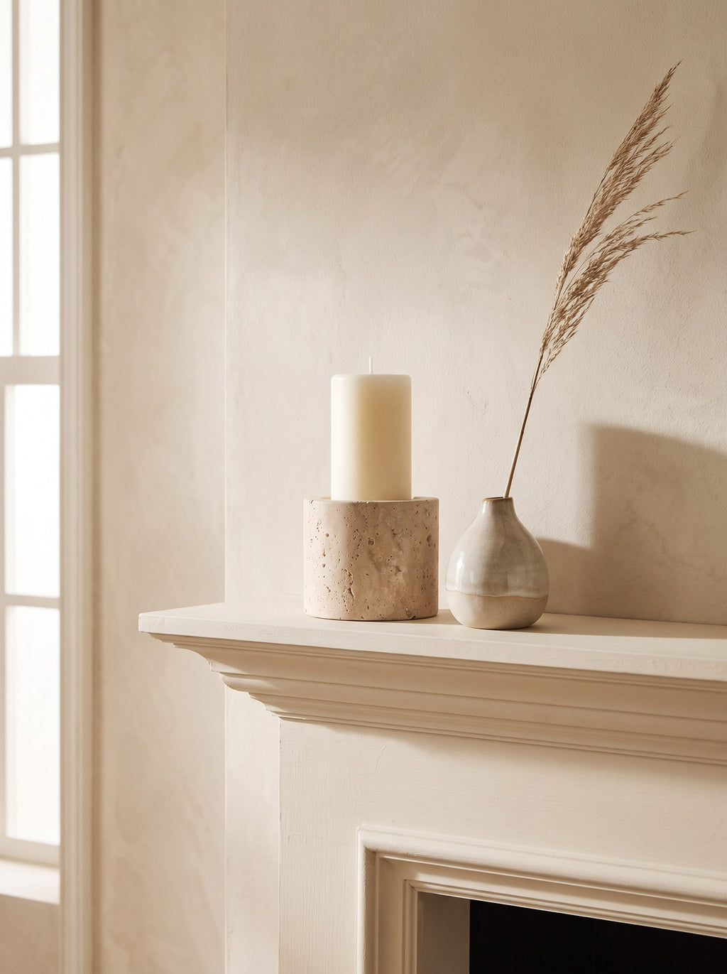 Travertine pillar candle holder on a mantelpiece beside a small vase